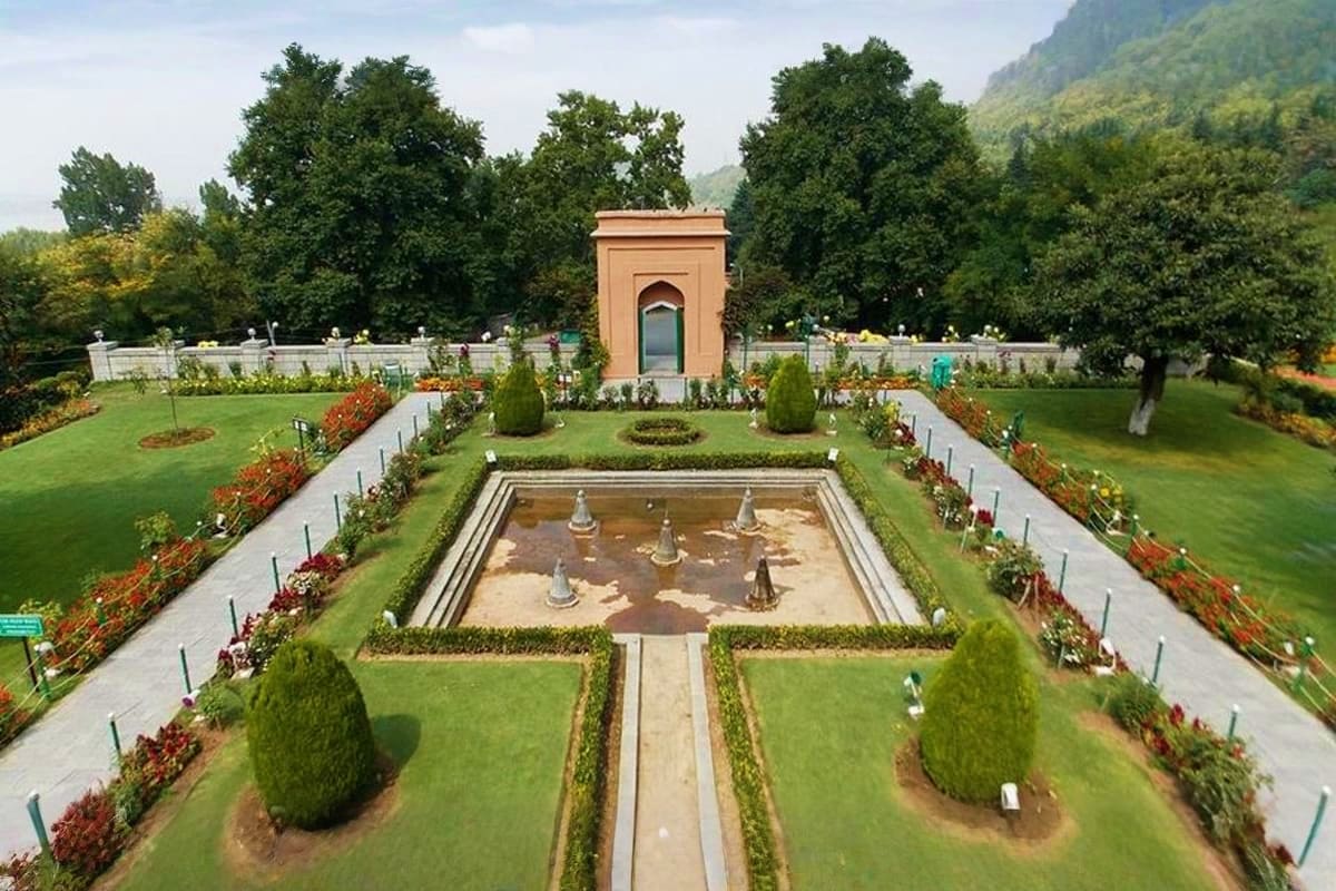 Formal Mughal garden with central rectangular water pool, manicured lawns, ornamental shrubs, and terracotta gatehouse buildi