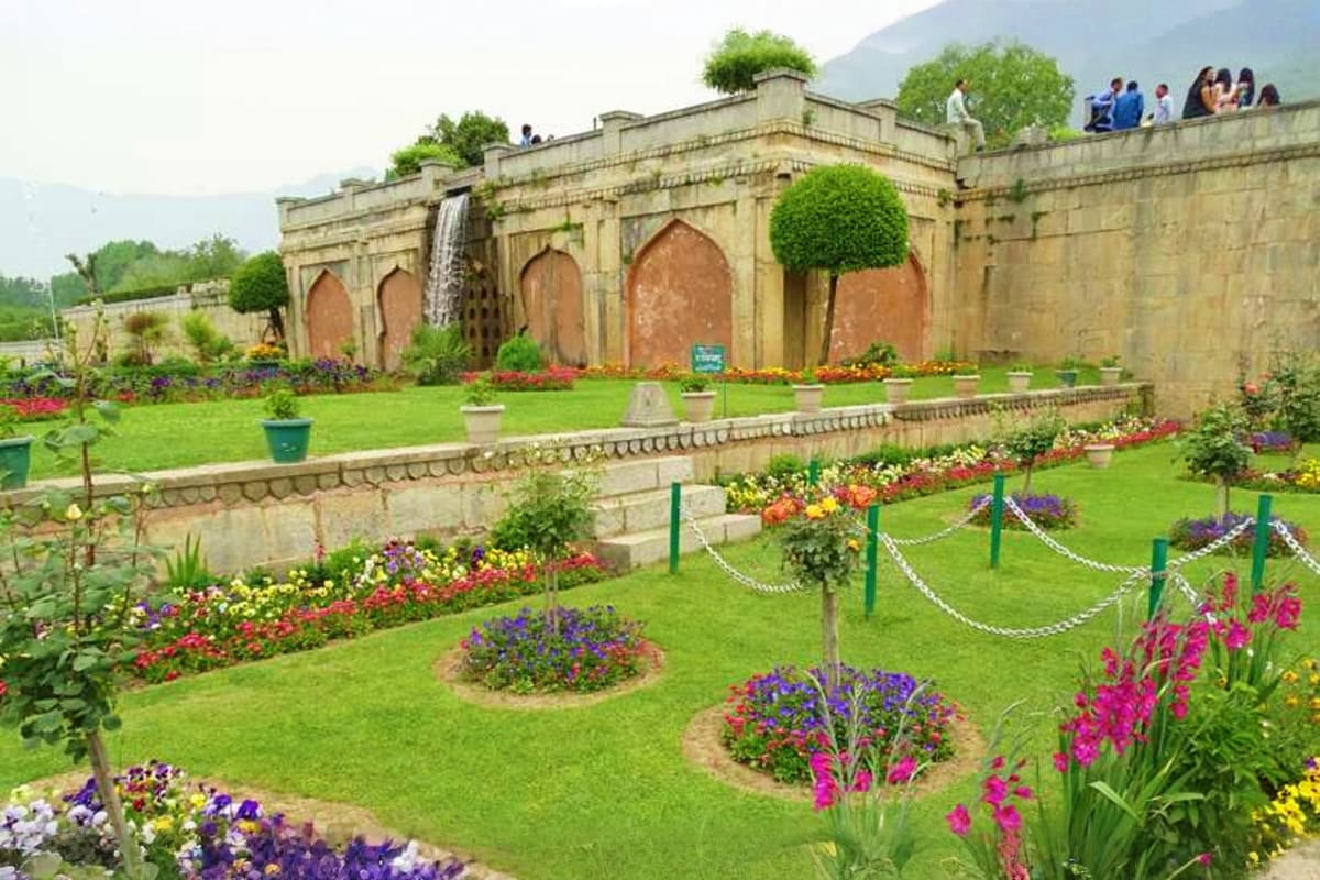 Shalimar Bagh garden in Kashmir with manicured lawns, colorful flower beds, and historic Mughal architecture with arched alco