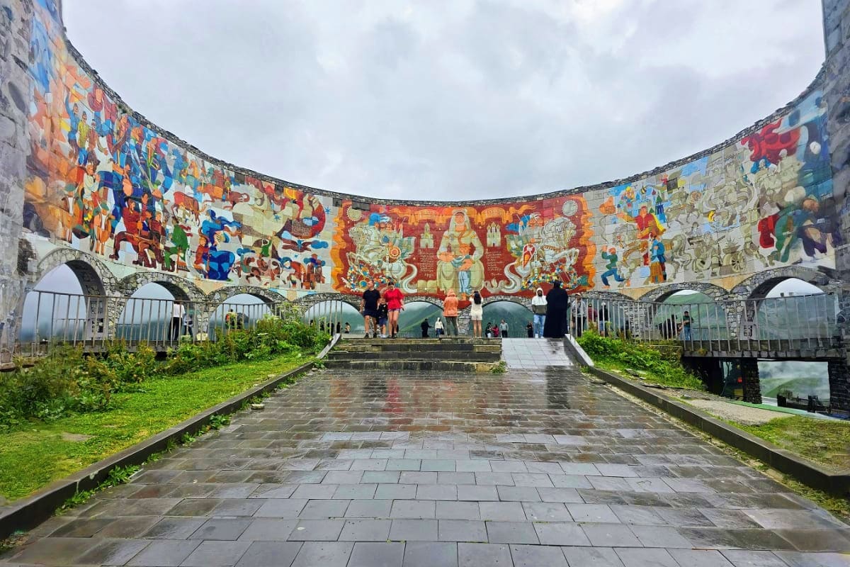 Circular ancient stone structure with colorful murals depicting traditional scenes, visitors walking on paved floor, arched o