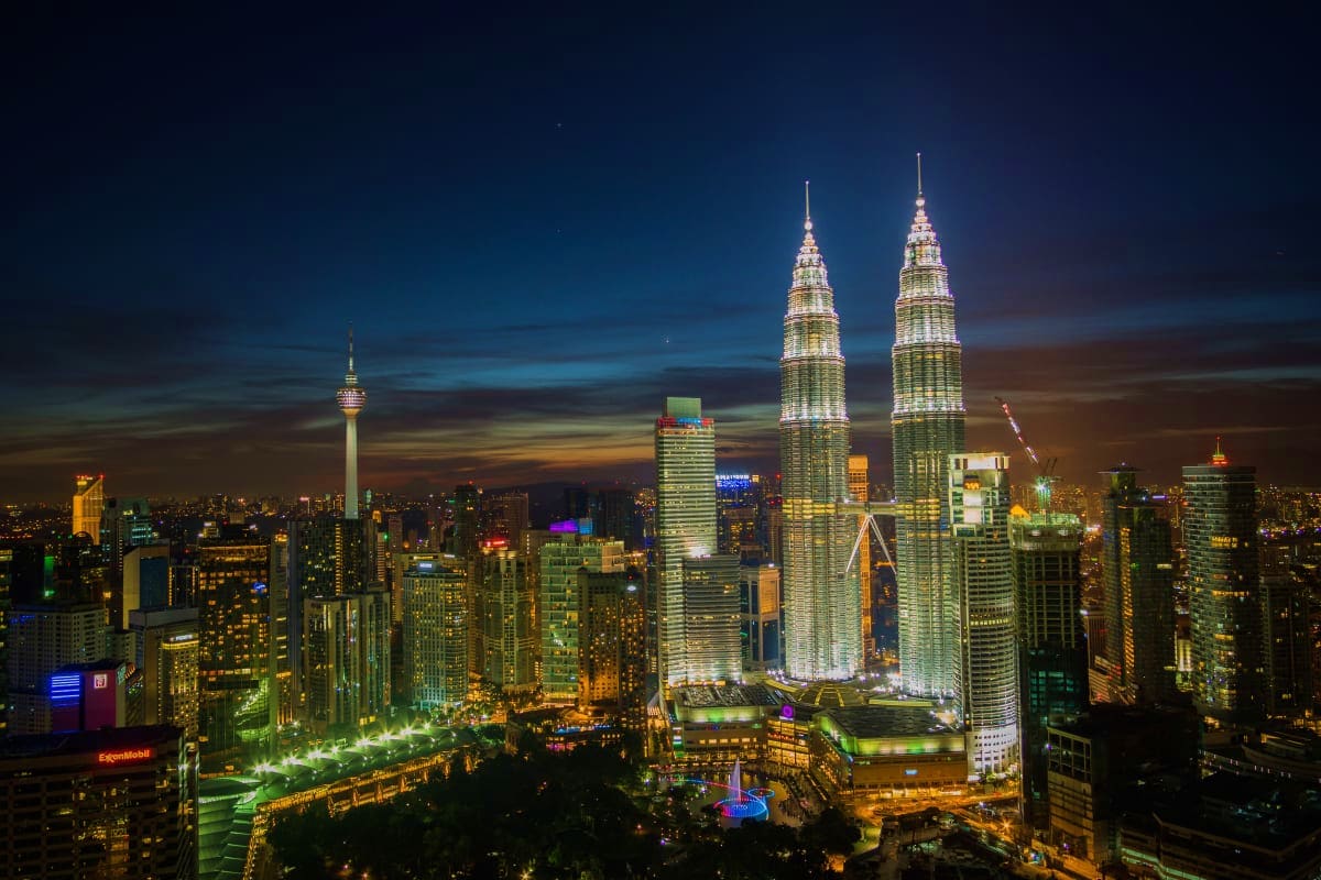Illuminated Petronas Twin Towers at night dominating the Kuala Lumpur skyline with surrounding city lights and buildings