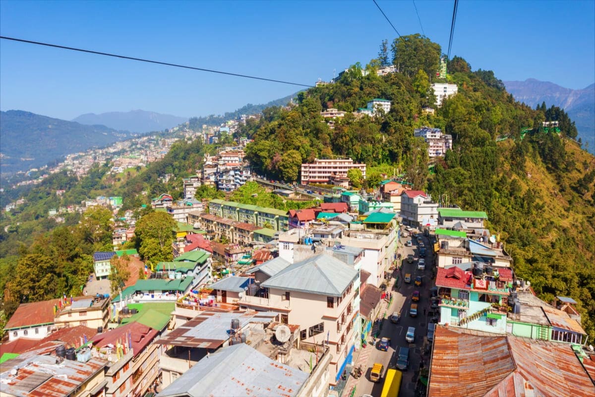 Aerial view of Namchi town nestled in forested Himalayan mountains with colorful buildings and winding roads on hillside terr