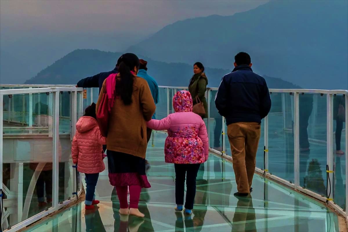 Family viewing mountainous landscape from glass skywalk overlooking misty lakes and forested valleys in Sikkim Himalayas