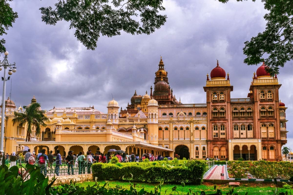 Thiruvananthapuram Palace with ornate yellow and red architecture, golden domes, visitors in courtyard, green gardens and tre