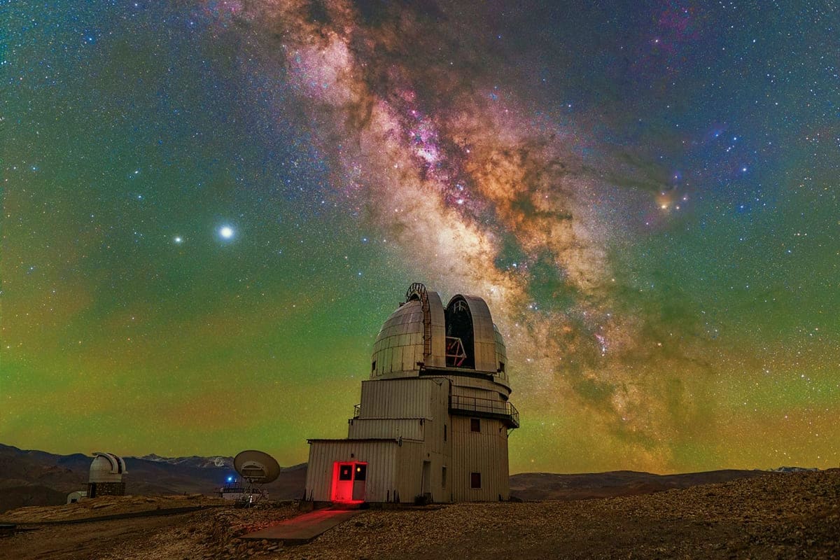 Observatory dome with red door silhouetted against Milky Way galaxy at night in desert landscape