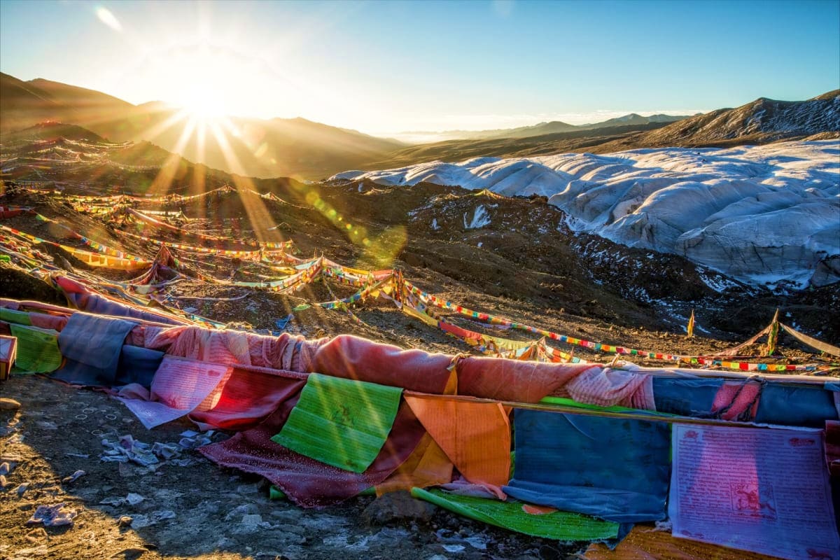 Prayer flags strung across mountainous Himalayan landscape at sunrise with snow-covered peaks and valley below in Ladakh