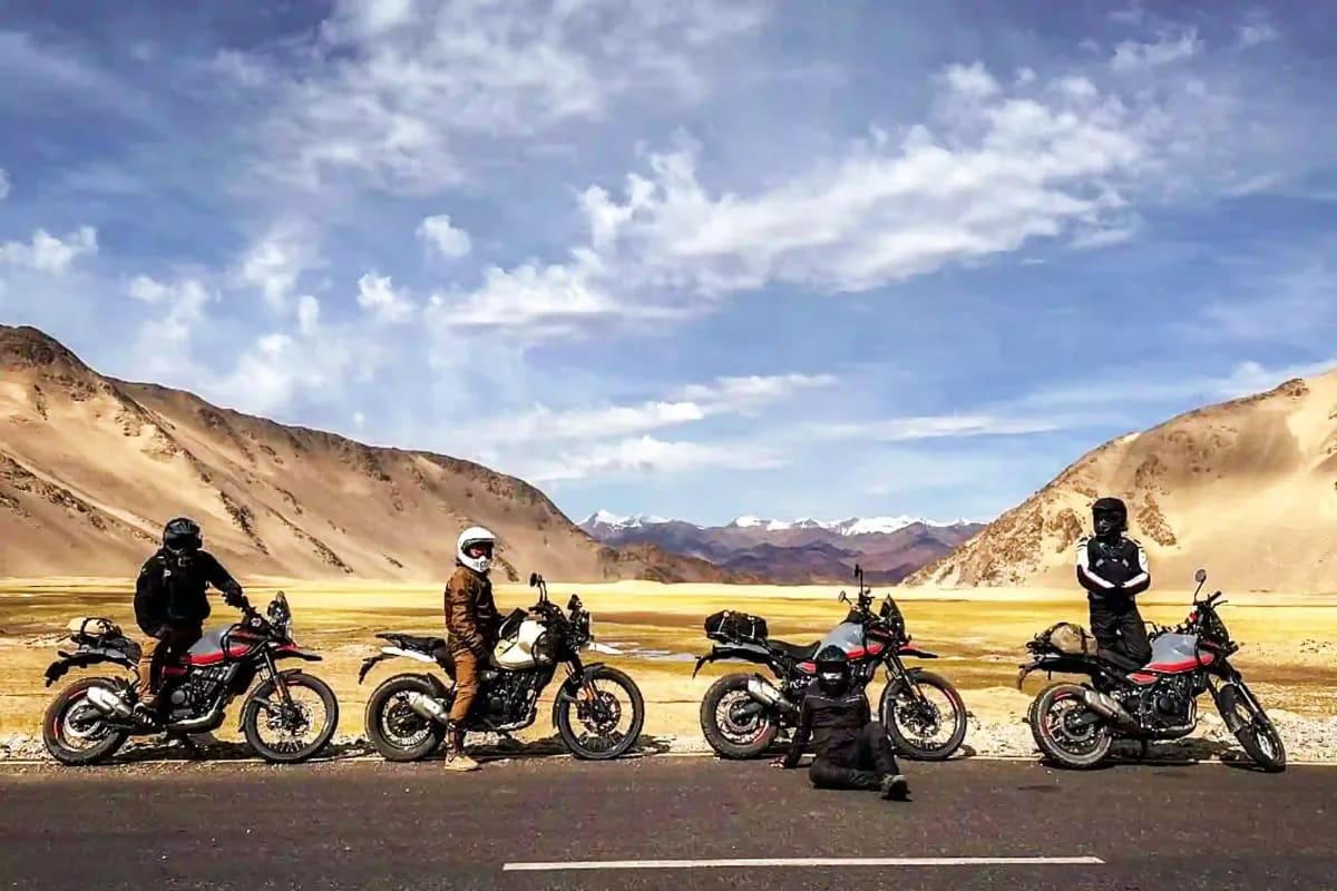 Group of motorcyclists standing with bikes on mountain road in high altitude desert valley with snow-capped peaks and yellow 