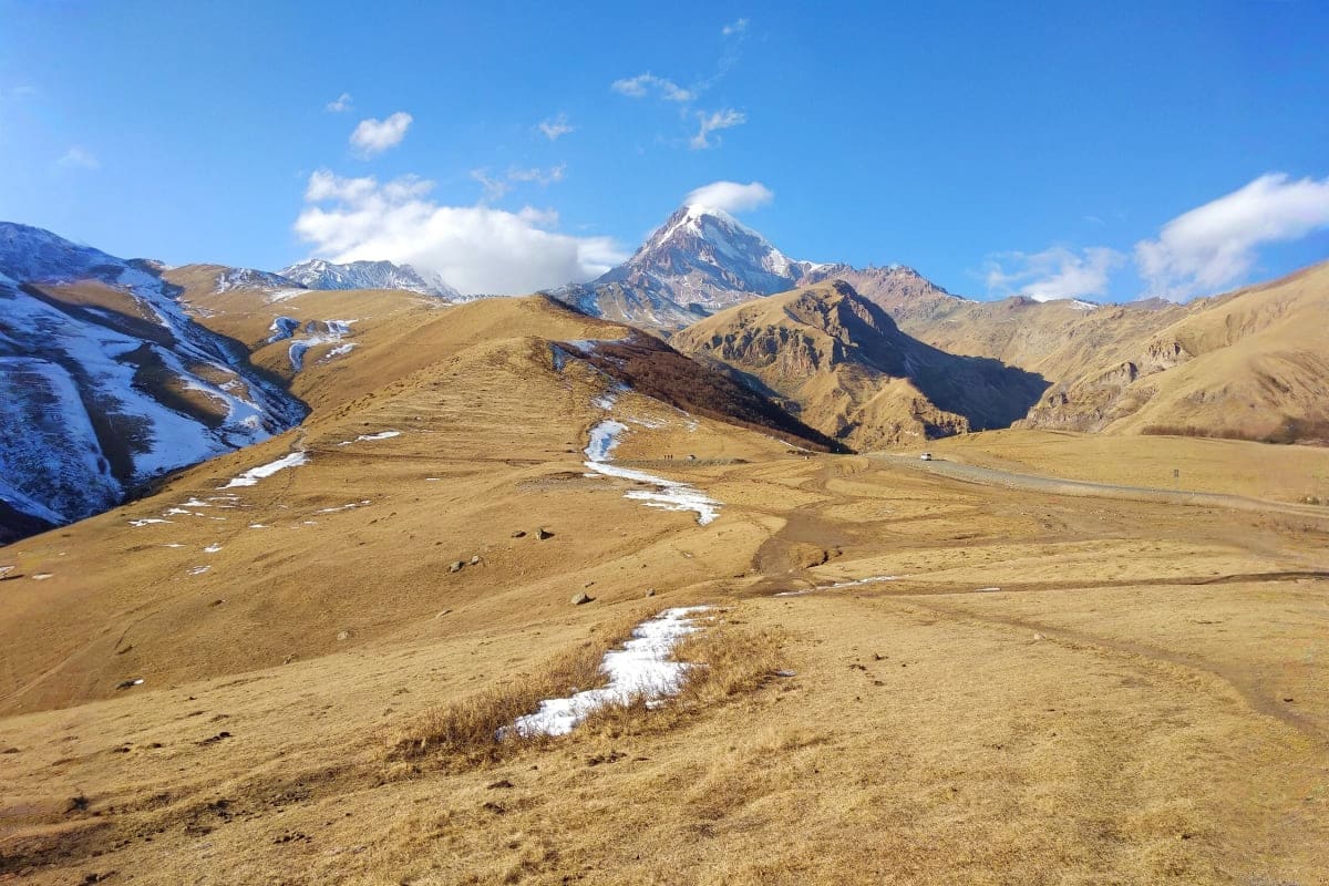 Snow-capped mountain peak rising above golden plateau with melting snow streams in Ladakh Himalayas