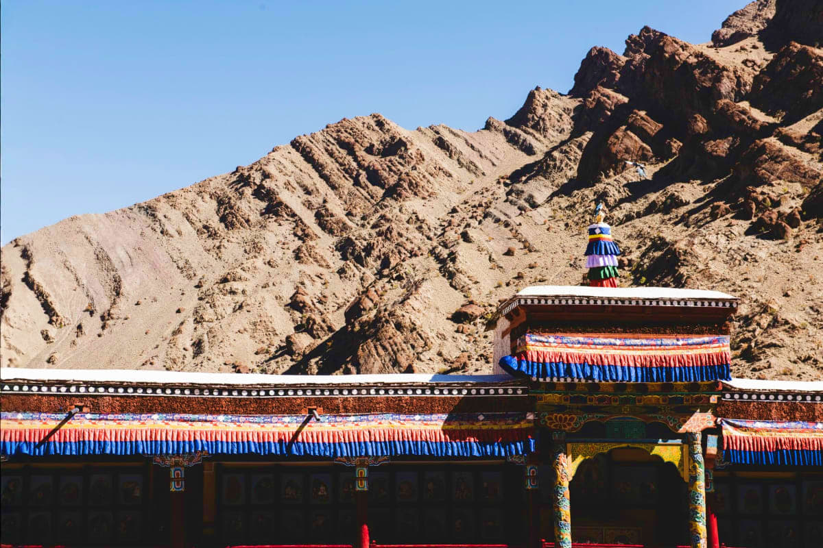 Tibetan Buddhist monastery with ornate blue and red roof against barren brown mountains in Leh Ladakh, India