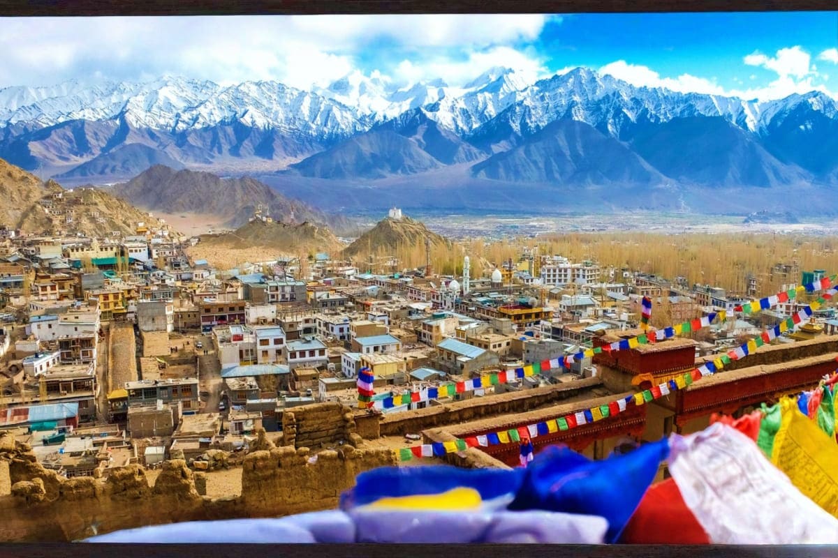 Leh Ladakh valley town with snow-capped Himalayan mountains in background and colorful Buddhist prayer flags in foreground