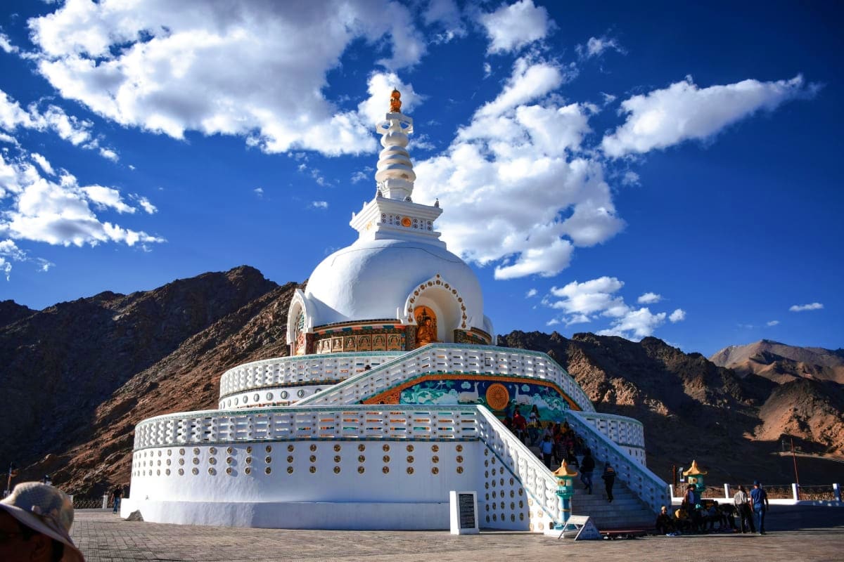 White Buddhist stupa with golden spire set against barren mountains and blue sky in Leh Ladakh