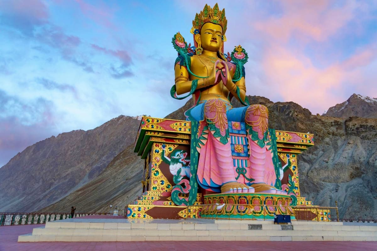 Towering golden Buddha statue with ornate temple base against rocky mountains at dusk in Ladakh, India