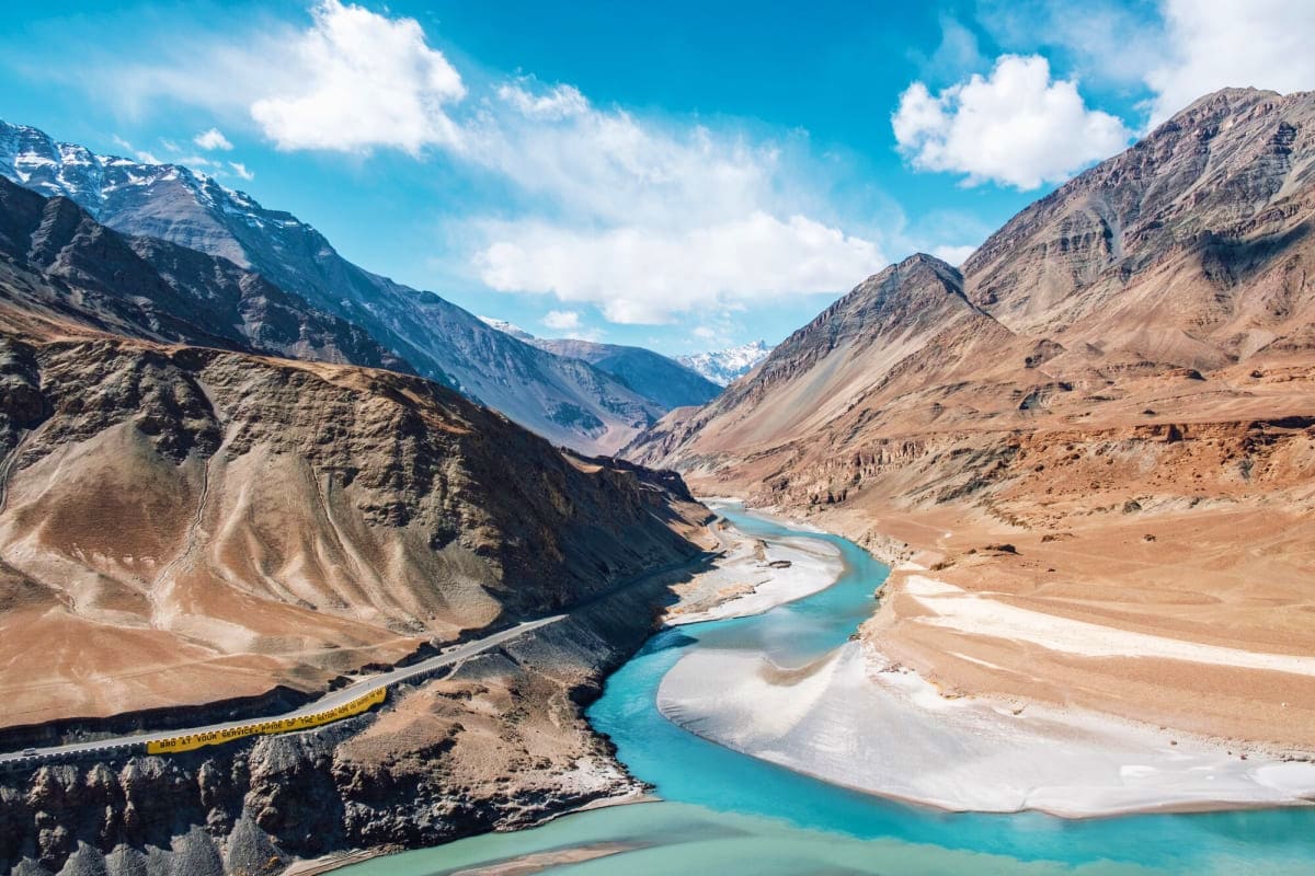 Turquoise river confluence in high altitude mountain valley with snow-capped peaks and barren terrain near Leh, Ladakh