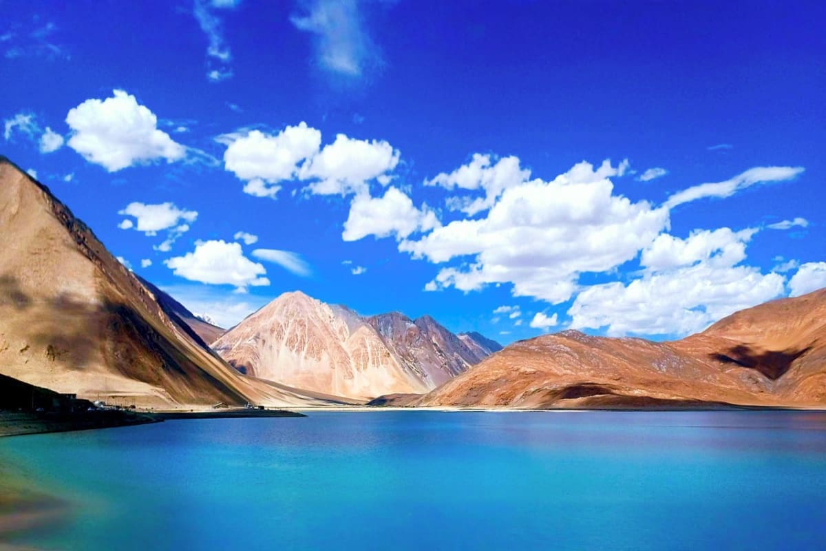 Turquoise alpine lake surrounded by barren mountains under blue sky with white clouds in Ladakh region