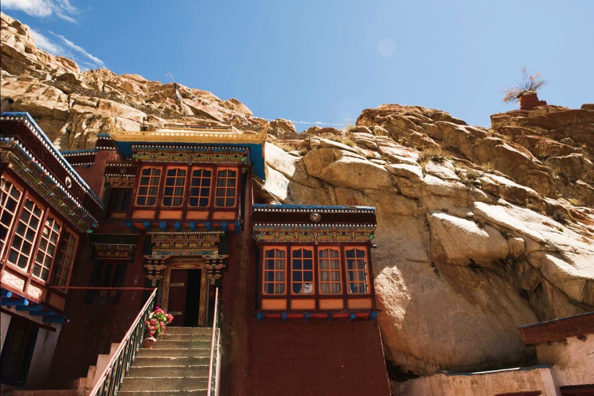 Traditional Tibetan Buddhist monastery with red walls and ornate blue trim built into steep rocky mountain cliffs in Leh, Lad