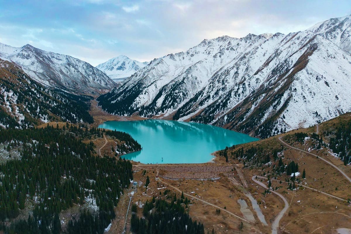 Turquoise alpine lake surrounded by snow-capped mountains and coniferous forests in Kazakhstan highlands