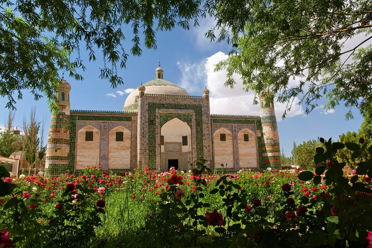 Historic mosque with turquoise tile dome and minarets surrounded by blooming red roses and willow trees in Uzbekistan