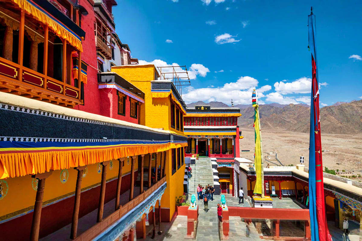 Colorful Tibetan Buddhist monastery with red and yellow buildings, prayer flags, and mountain landscape in Ladakh, India