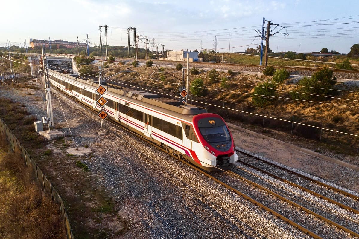 Modern red and white high-speed train on railway tracks in Uzbekistan with overhead power lines and industrial landscape