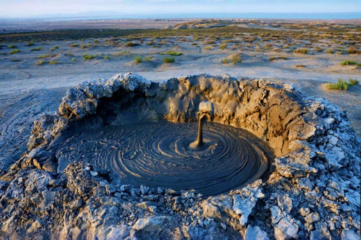 Aerial view of Mud Volcano in Azerbaijan with swirling dark mud patterns and rocky crater rim surrounded by arid landscape