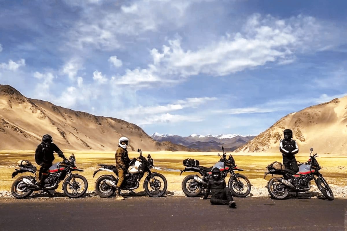 Group of motorcyclists with bikes lined up on a mountain road in a high-altitude desert valley with snow-capped peaks in the 