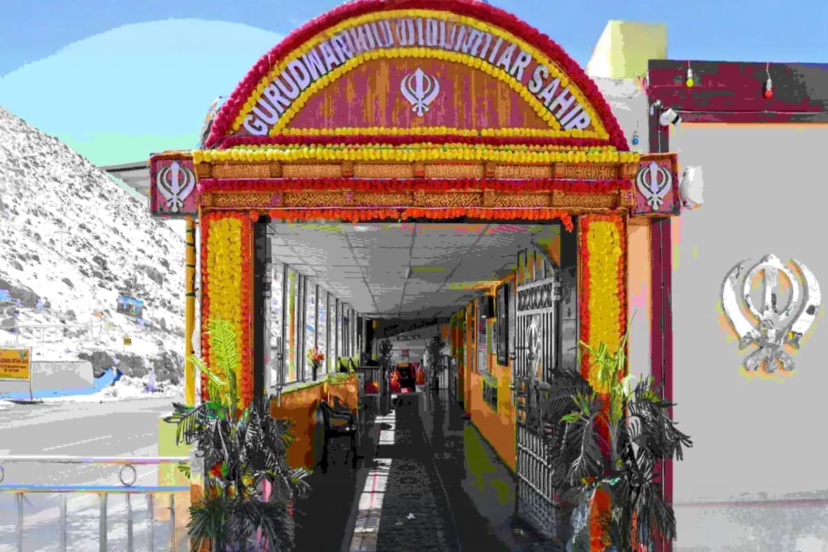 Ornate Sikh gurdwara entrance with red and yellow decorative arch and Khanda symbol in mountainous Ladakh region