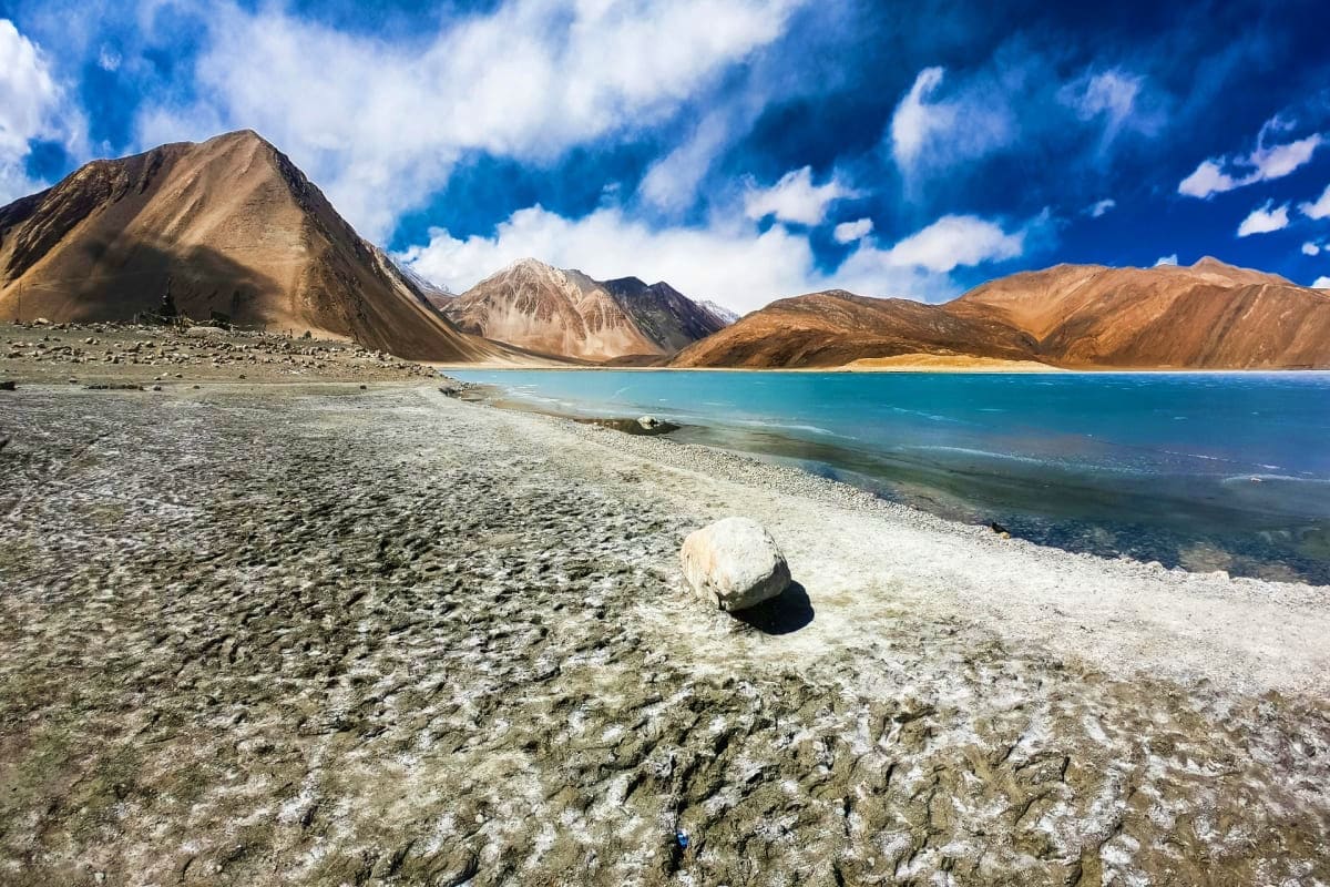 Pangong Lake with turquoise waters, salt-encrusted shore, and barren brown mountains under blue sky in Ladakh