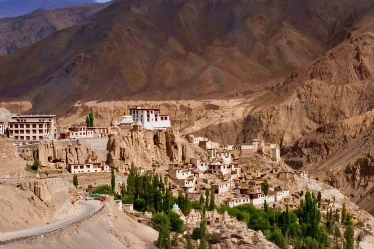 Lamayuru Monastery perched on rocky cliffs in Ladakh with white-walled buildings, golden roofs, and poplar trees in a desert 