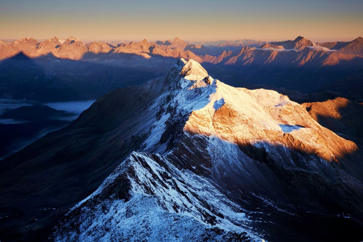 Snow-covered alpine peak at sunrise with vast mountain range and valley below in the Ladakh region