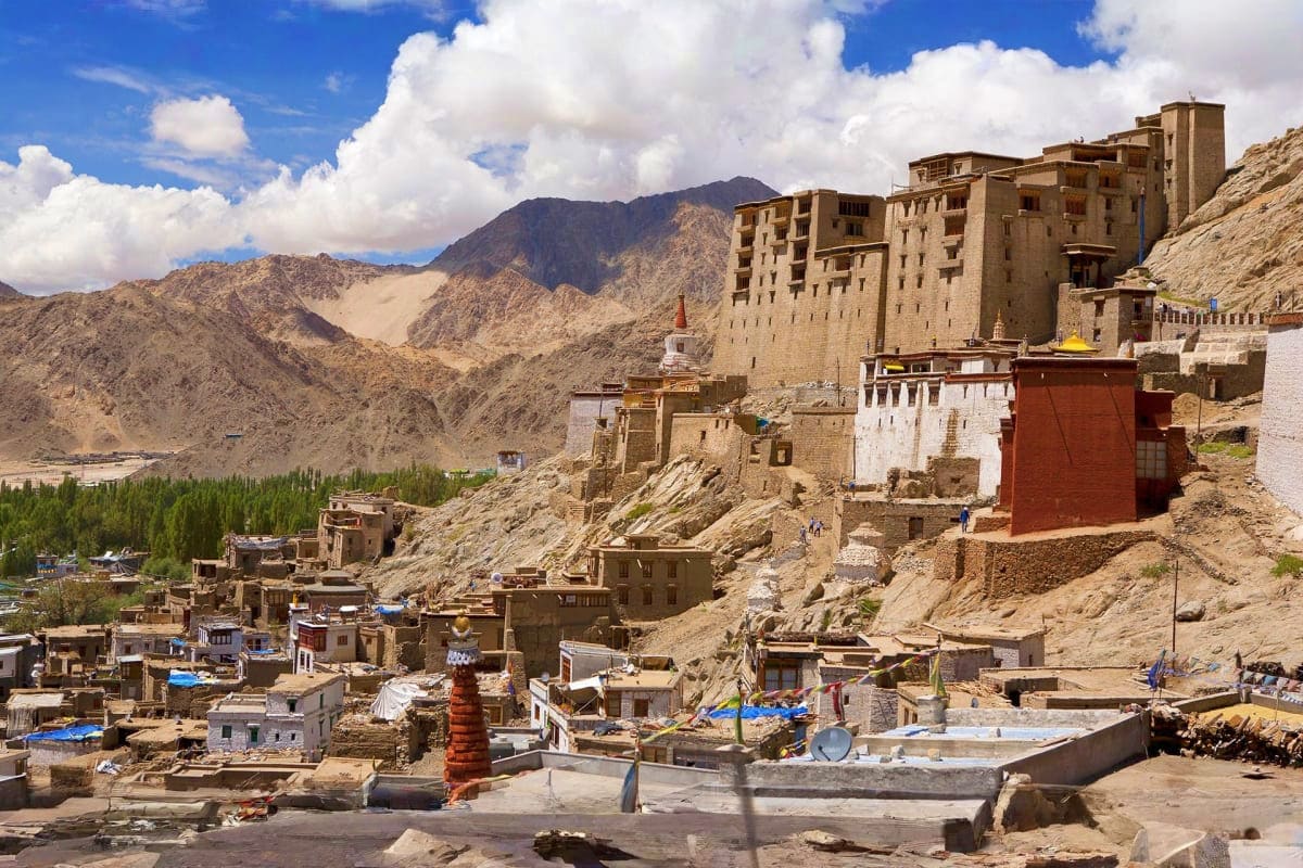 Thiksey Monastery perched on mountainside in Ladakh with traditional stone buildings, barren peaks, and blue sky with clouds