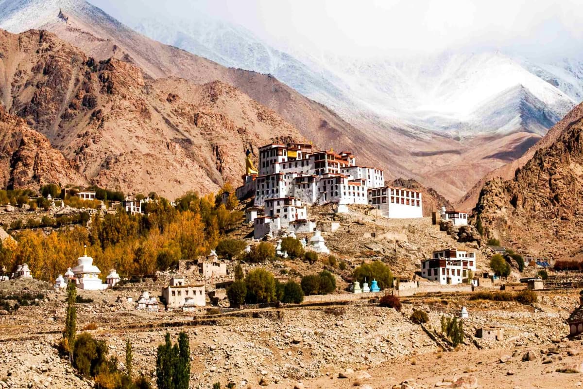 Tibetan Buddhist monastery with white and dark wooden buildings perched on rocky mountainside in Ladakh valley with snow-capp