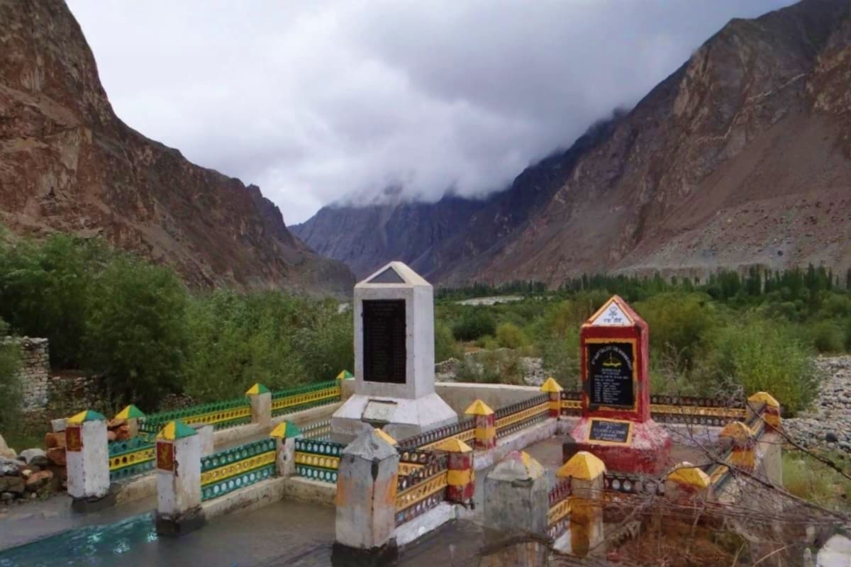 Mountain shrine with white and red structures surrounded by colorful fencing in a high-altitude valley with snow-capped peaks