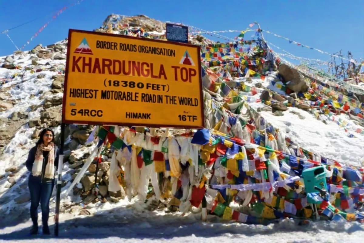 Tourist at Khardungla Top sign marking world's highest motorable road at 18380 feet in Ladakh with colorful prayer flags on s