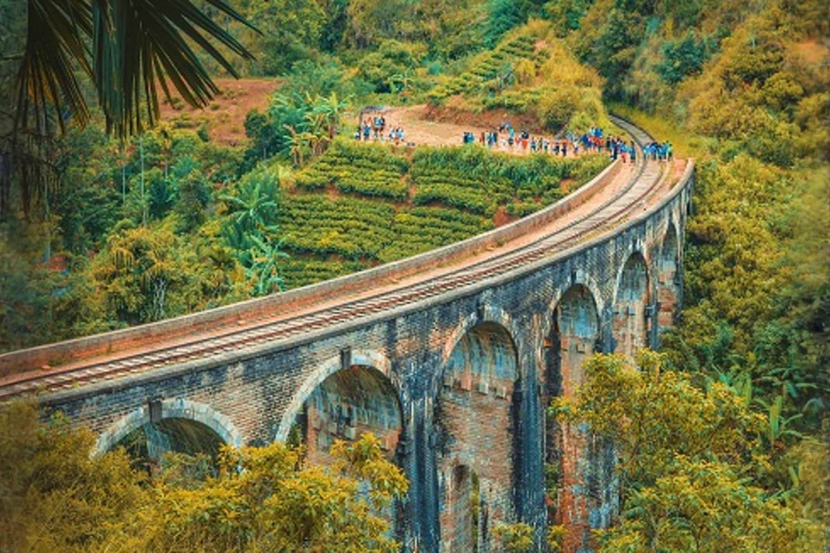 Historic stone railway viaduct with multiple arches crossing through lush green hills and tea plantations in Sri Lanka, with 