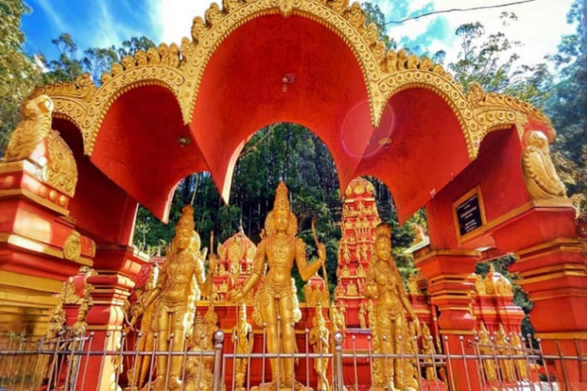 Golden Buddhist statues displayed in front of a red and gold ornate temple shrine with carved archways and forest backdrop