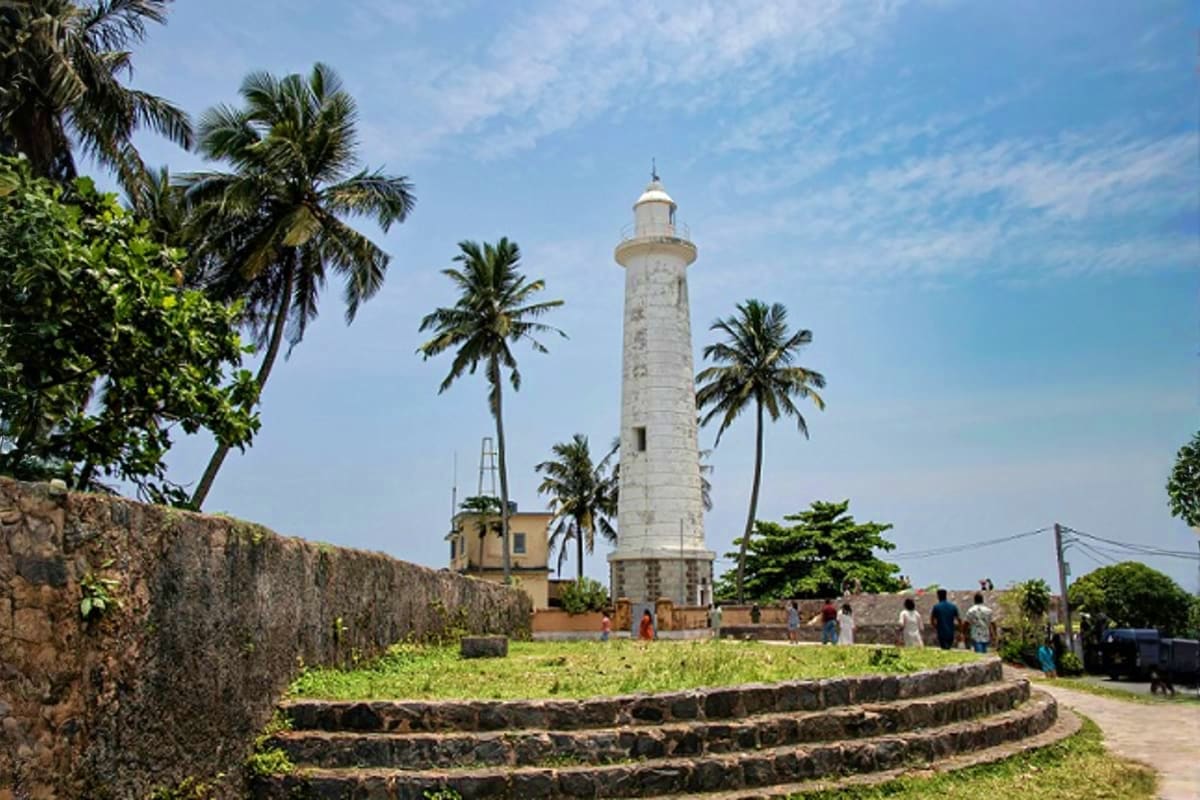 Historic white lighthouse surrounded by palm trees and stone fortifications on tropical island