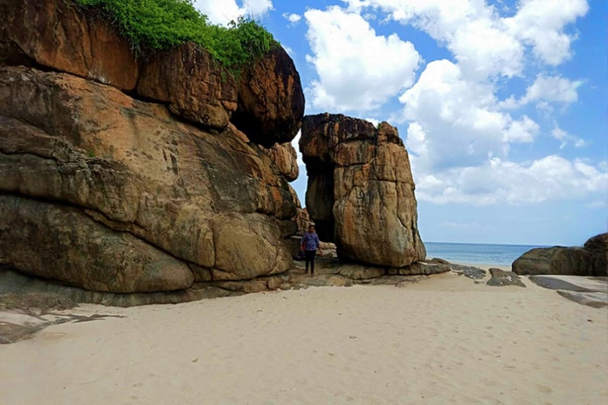 Tourist walking between two large granite rock formations on sandy beach with ocean and blue sky in background