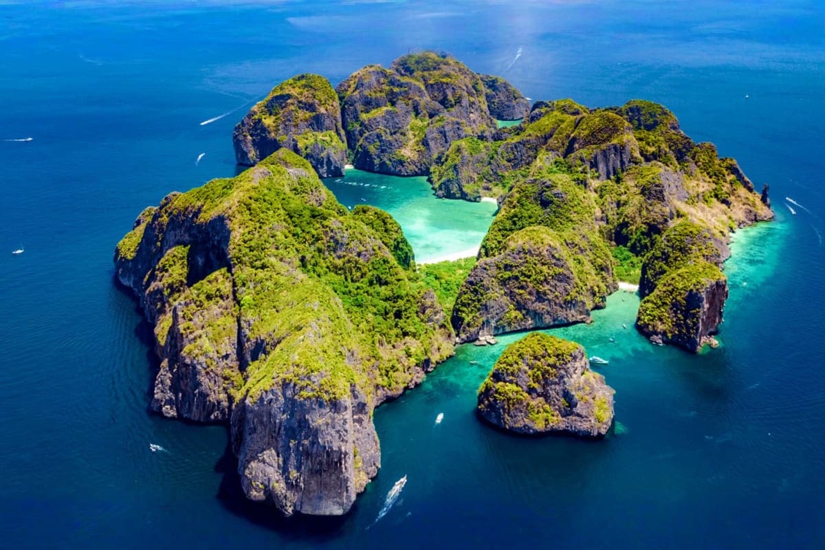Aerial view of limestone cliffs and turquoise lagoons in Phang Nga Bay, Thailand with lush green vegetation and small boats