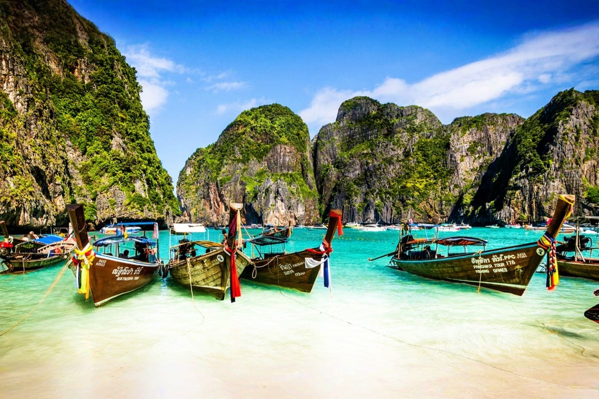 Traditional longtail boats anchored in turquoise water with limestone cliffs at Maya Bay, Thailand