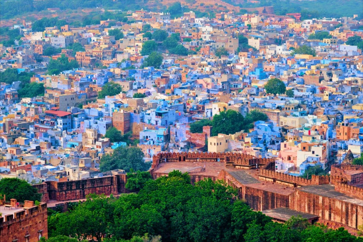 Experience Jaisalmer Desert Camps and Fort Visits of Rajasthan Aerial view of Jaisalmer's blue and golden cityscape with historic fort walls and dense residential buildings nestled in the