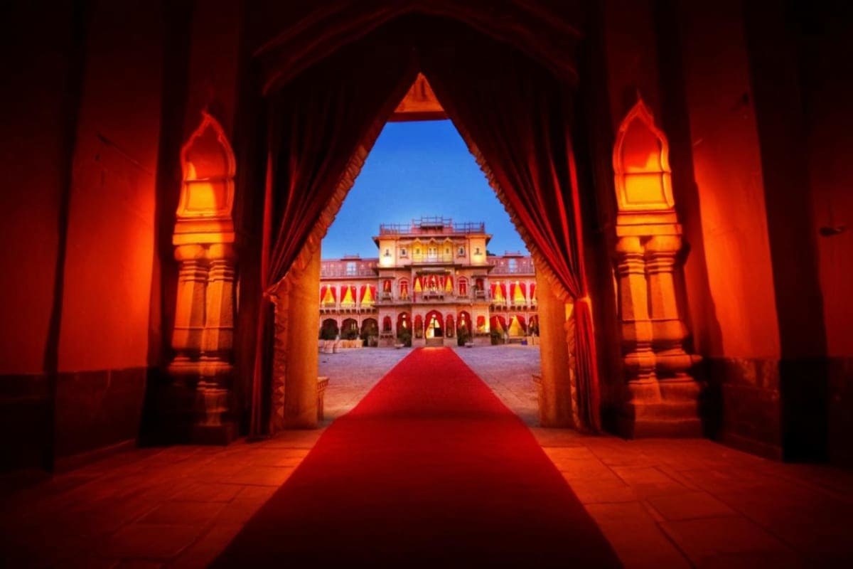 Experience Jaisalmer Desert Camps and Fort Visits of Rajasthan Red carpet leading through ornate palace archway with illuminated lanterns toward golden Jaisalmer Fort facade with flags und
