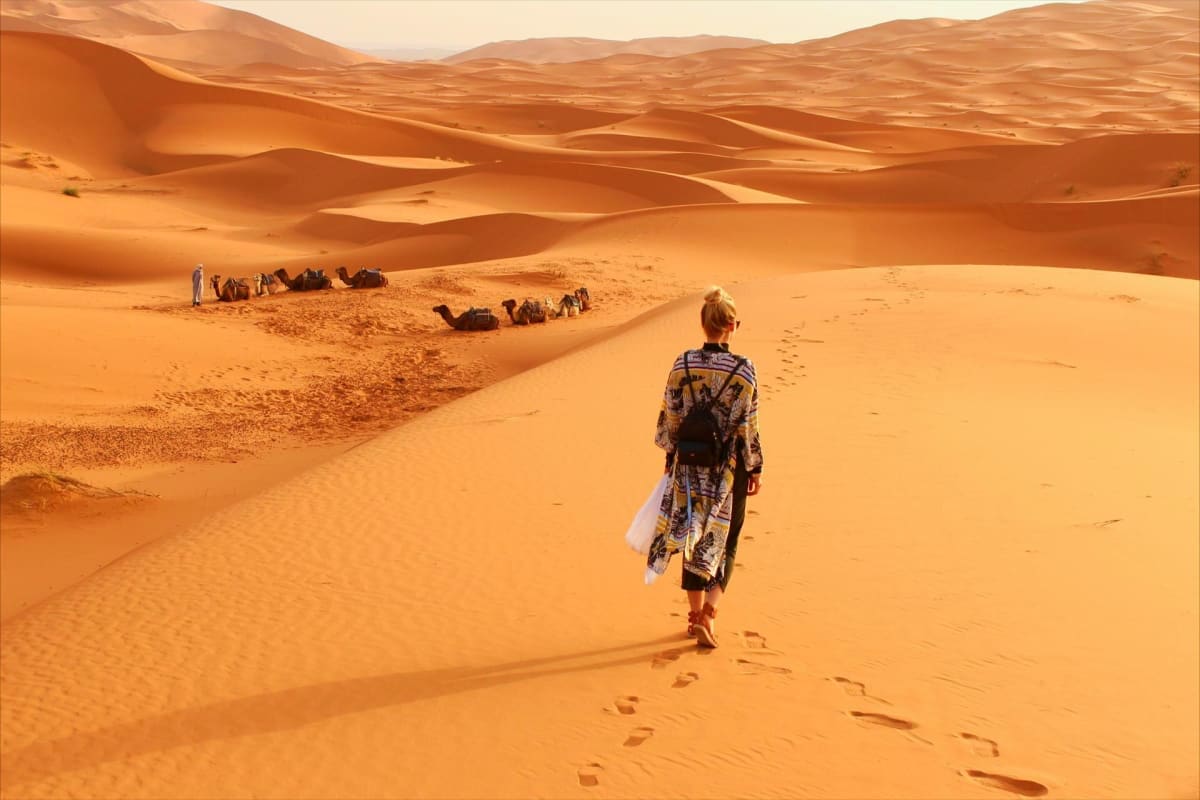Experience Jaisalmer Desert Camps and Fort Visits of Rajasthan Tourist walking across golden sand dunes toward camel caravan camp in Jaisalmer Desert, Rajasthan