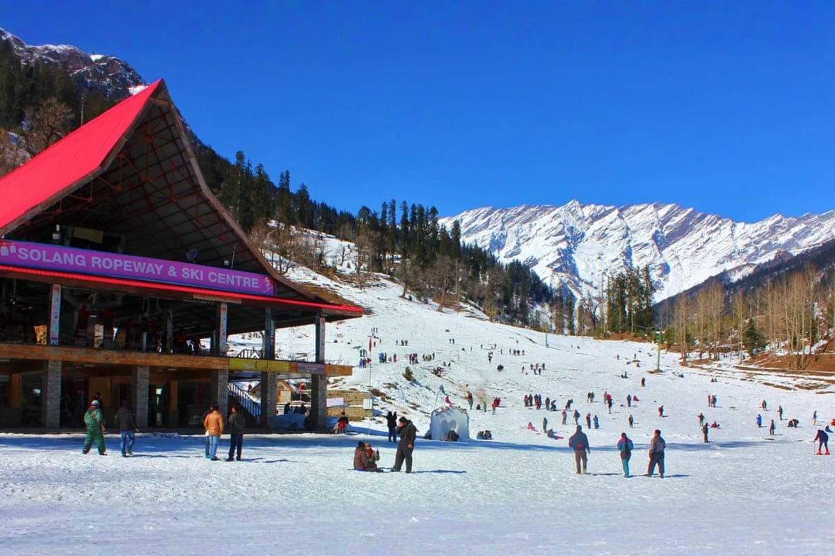 Solang Ropeway and Ski Centre in Manali with snow-covered slopes, visitors on snowy ground, pine forests, and snow-capped mou