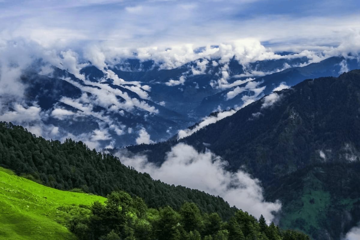 Alpine valley with forested slopes and white clouds in Himachal Pradesh mountains during monsoon season