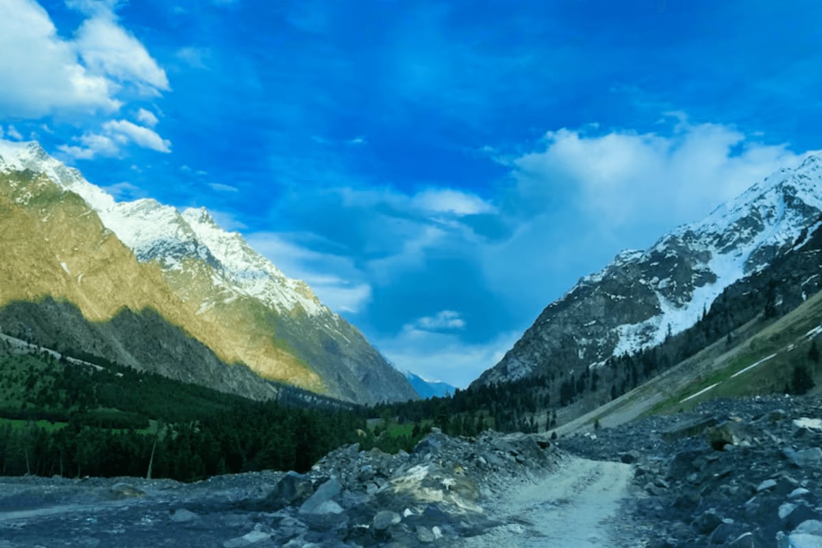 Snow-capped mountain valley with forested slopes, rocky terrain and clear blue sky in Himachal Pradesh hill region