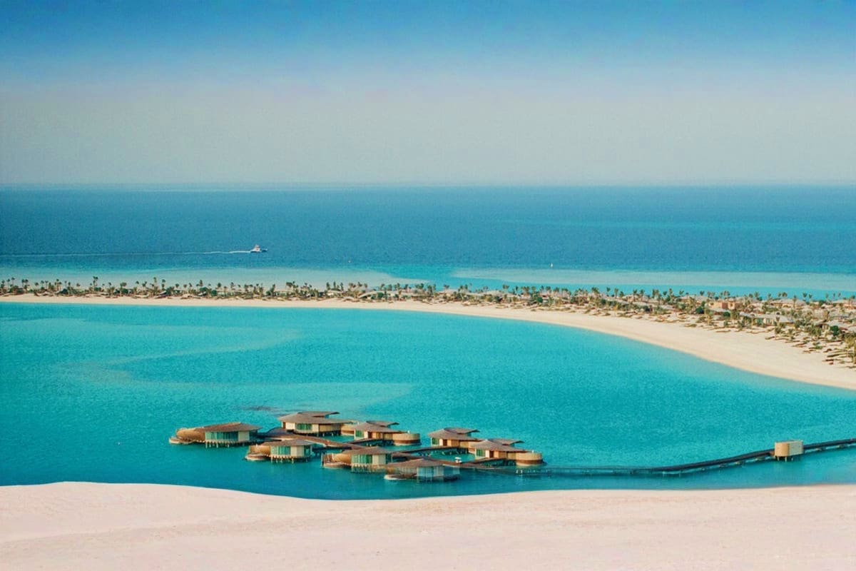 Aerial view of overwater bungalows in turquoise lagoon with pristine white sand beach and palm trees along the Red Sea coastl
