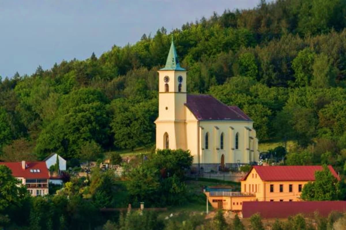 Historic yellow church with green spire surrounded by forested hills and traditional houses near a river in the Himalayas