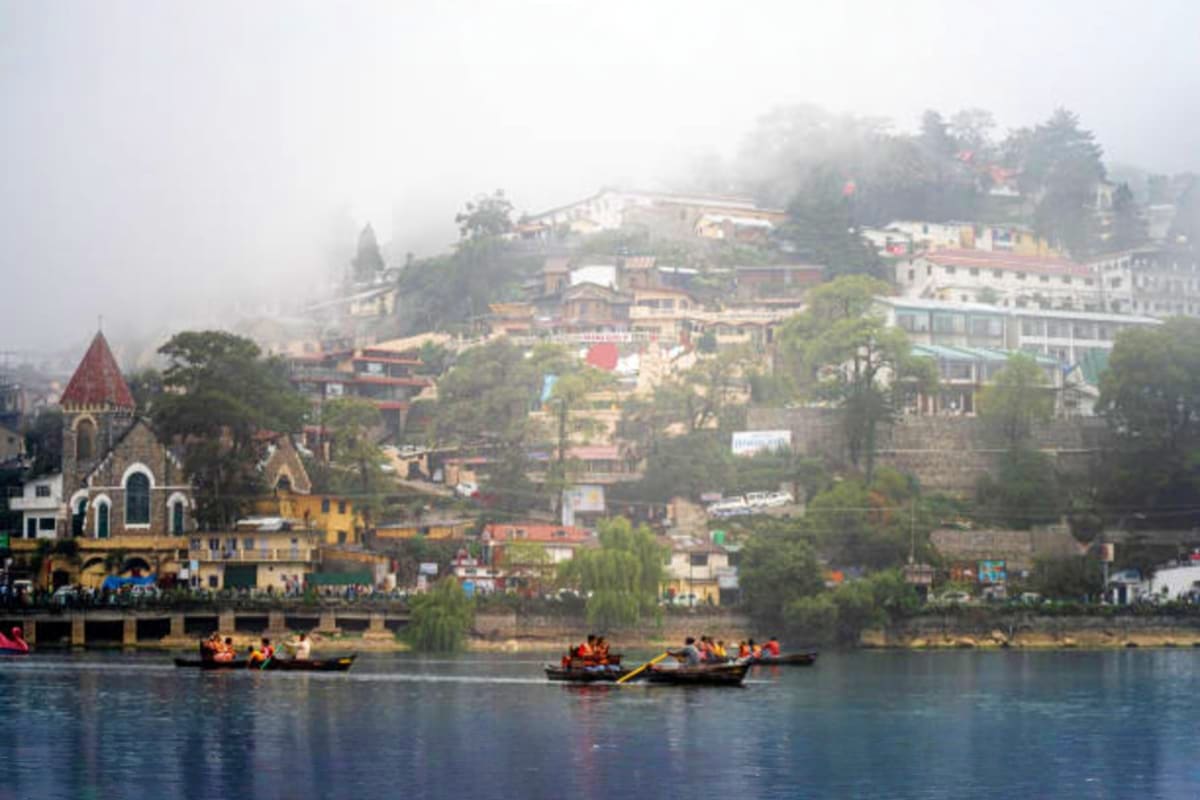 Misty morning view of Nainital with traditional wooden boats on the lake, hillside buildings, and a church with red roof nest