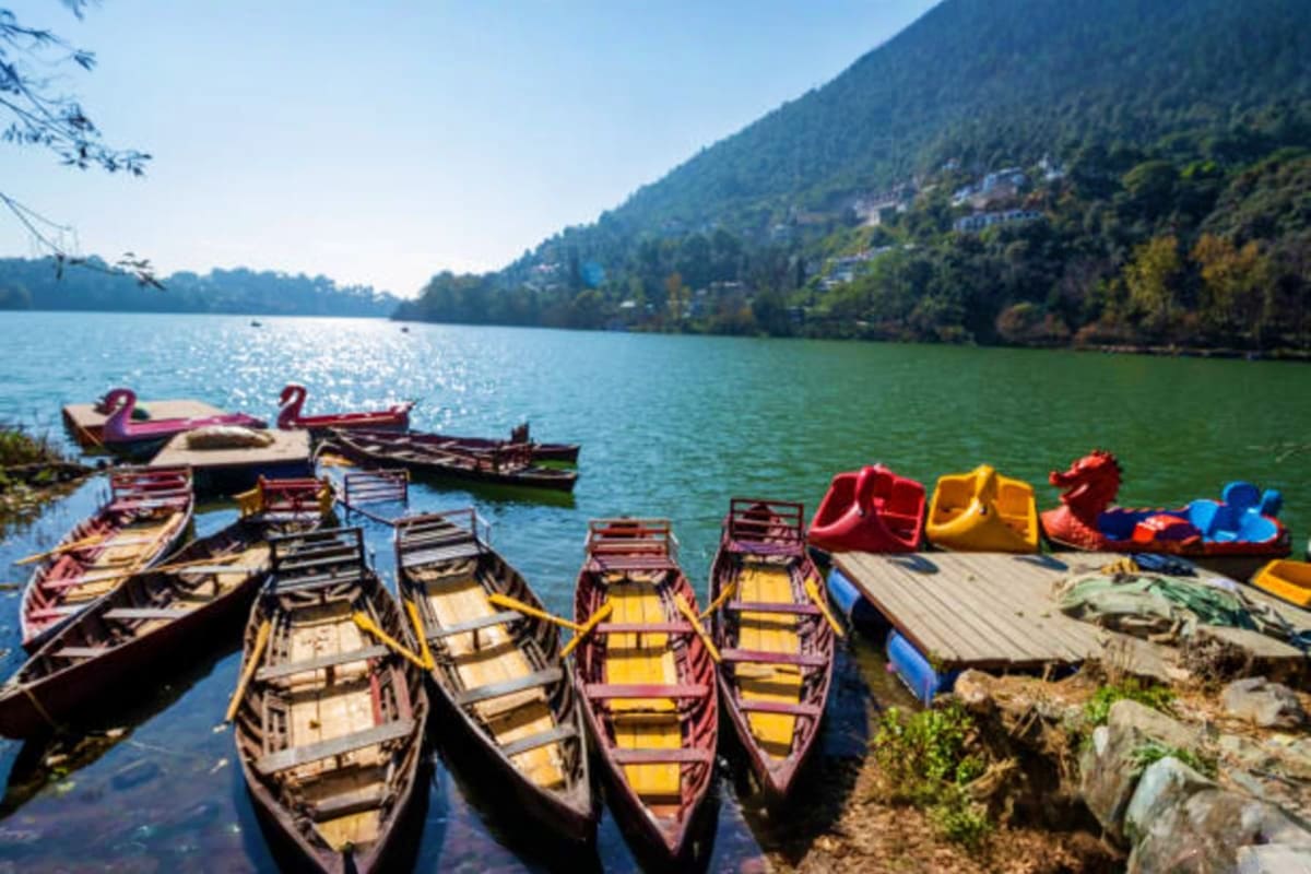 Colorful wooden boats lined up at the shore of Nainital Lake with forested mountains in the background