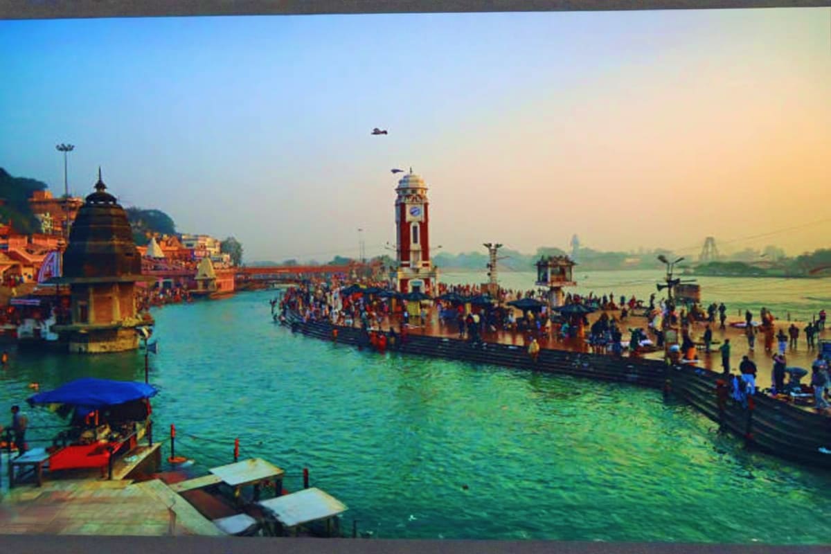 Crowded ghats along the Ganges River in Haridwar with temples, clock tower, and pilgrims gathered for religious ceremonies at