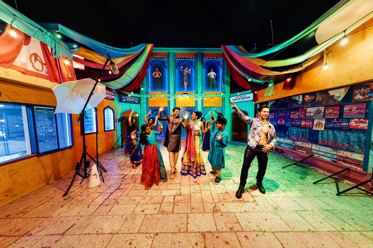 Singapore-Family-Fun-Package Colorful indoor exhibition space with visitors in traditional Indian attire celebrating, featuring bright blue and green arch